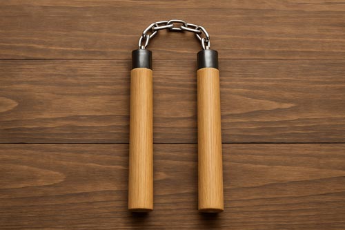 A pair of wooden nunchucks with a metal chain connector displayed on a wooden surface.