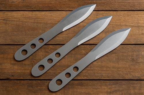 Blade-heavy throwing knives displayed on a wooden surface