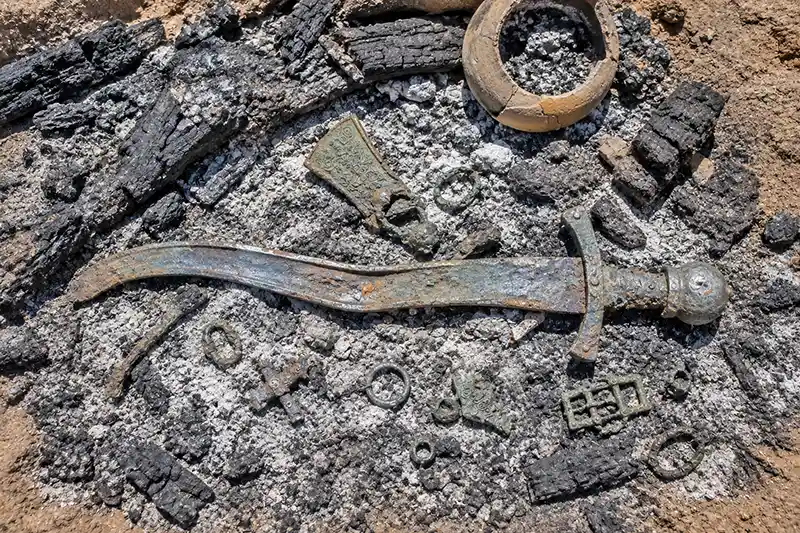 Heat-warped ancient sword among cremation pyre remains