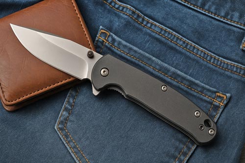 Folding pocket knife resting on denim jeans with a brown leather wallet.