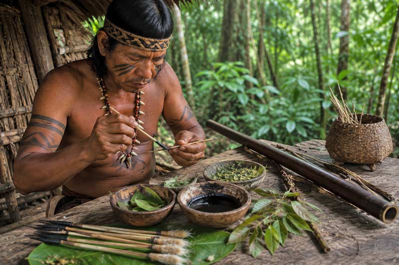 Traditional hunter preparing blowgun darts with natural plant extracts in a rainforest shelter