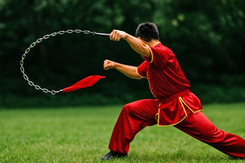 martial artist in red kung fu uniform swinging a chain whip outdoors