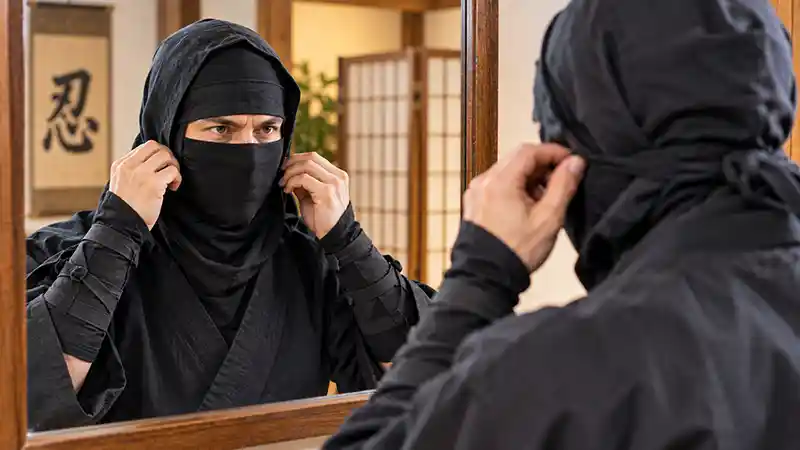 Ninja adjusting face mask in front of mirror.