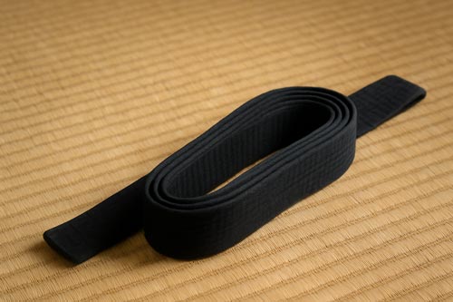 rolled up black belt laying on a tatami mat
