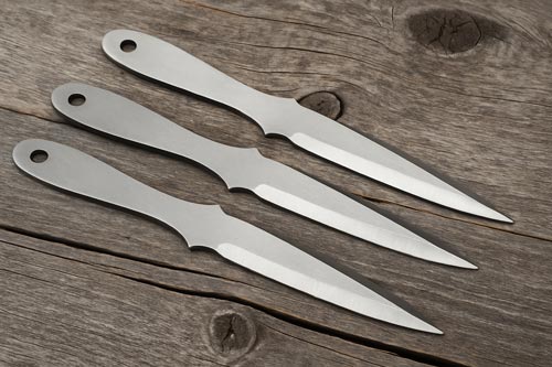 Straight throwing knives arranged on a wooden surface
