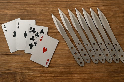 Throwing cards and throwing knives displayed on a wooden surface