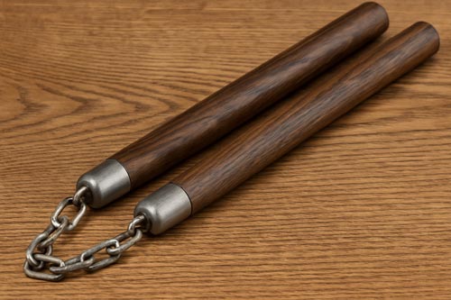 A pair of traditional wooden nunchucks with metal chain connectors resting on a wooden table.