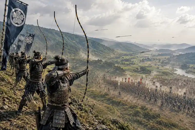 Samurai archers on a hillside firing a coordinated volley of yumi arrows toward an advancing army below.
